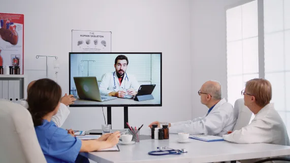 A medical team in a meeting room watching an HCP webinar on a screen.
